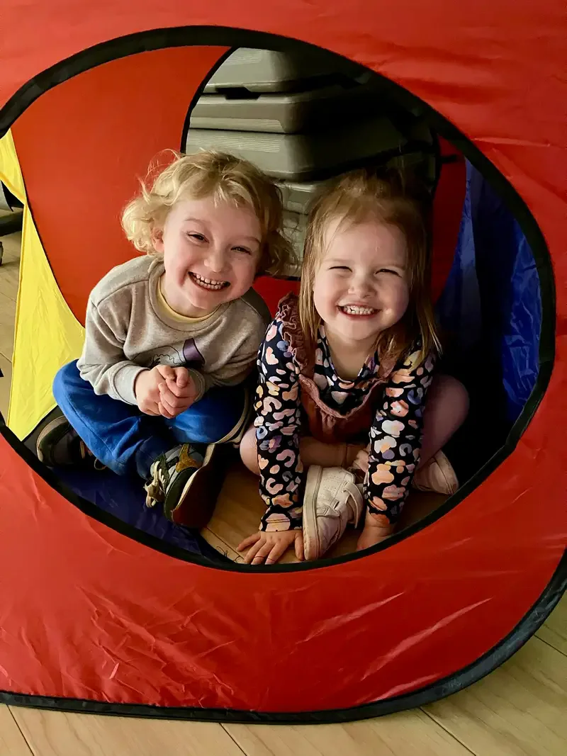 Two smiling children peeking from a play tunnel at Track Tots